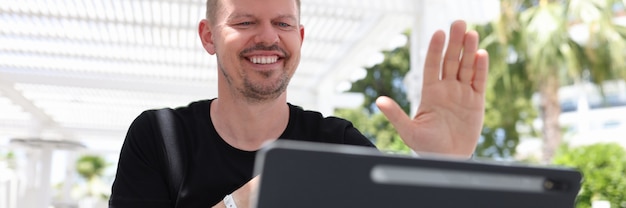 Retrato de hombre sonriente saludando a la pantalla de la tableta mientras está sentado afuera en los trópicos