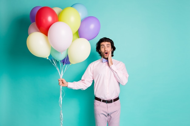 Retrato de hombre sonriente sorprendido con la boca abierta toque el pómulo vestido camisa formal pantalones sostienen globos de colores aislados sobre fondo de color turquesa