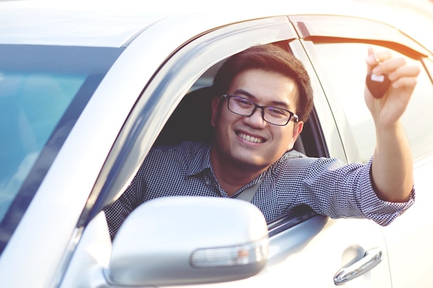 Foto retrato de un hombre sonriente sosteniendo la llave mientras está sentado en el coche
