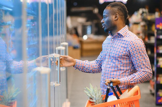 Retrato de un hombre sonriente en un supermercado Un joven africano con una canasta de compras en una tienda de comestibles