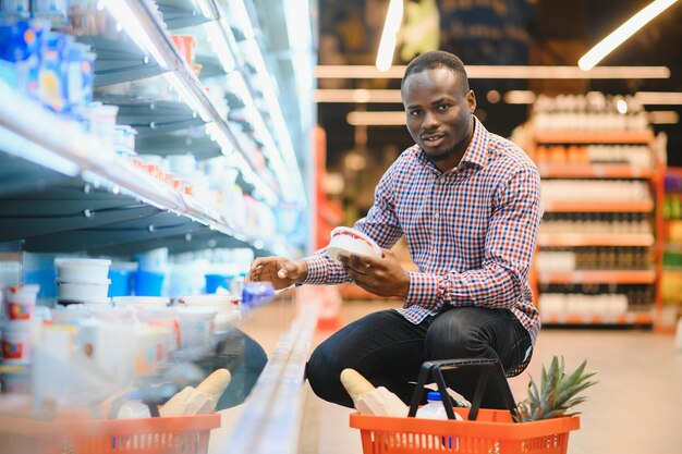 Retrato de un hombre sonriente en un supermercado Un joven africano con una canasta de compras en una tienda de comestibles