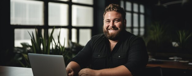 Retrato de un hombre sonriente de talla grande cerca de la computadora portátil en la oficina