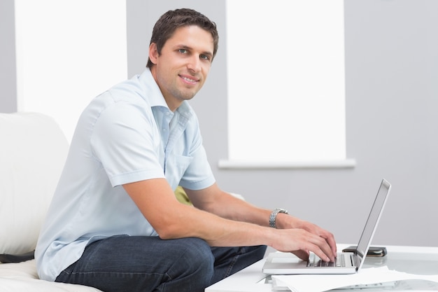 Retrato de hombre sonriente usando la computadora portátil en la sala de estar