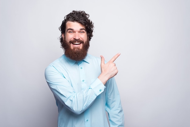 Retrato de hombre sorprendido con barba vistiendo camisa azul y apuntando hacia afuera.