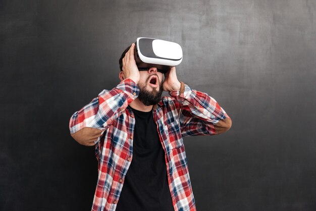 Retrato de hombre sorprendido vestido con camisa en una jaula y con dispositivo de realidad virtual de pie en la pizarra