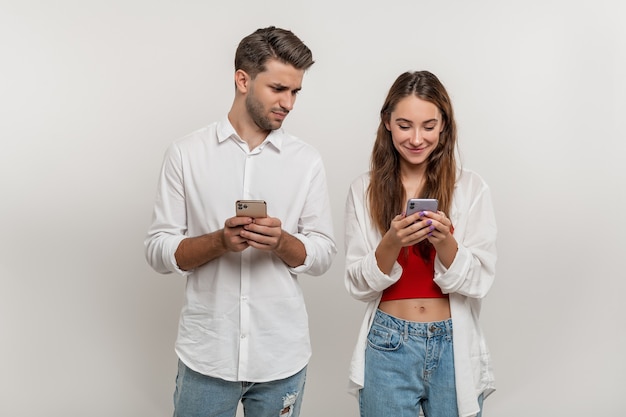 Foto retrato de hombre sospechoso espiando a su novia feliz mediante teléfono móvil aislado sobre blanco