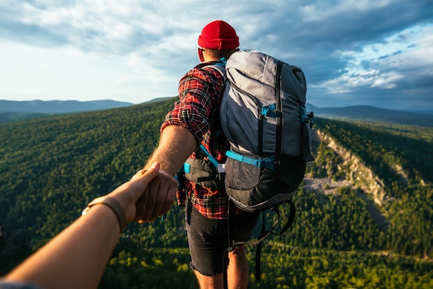 Retrato de un hombre sosteniendo la mano de su mujer mientras caminaba por una cordillera. La pareja disfruta de un paseo por la naturaleza. Una niña sostiene la mano de su novio en las montañas. Un viaje a la montaña