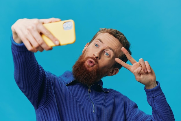 Retrato de un hombre con un teléfono en sus manos blogger toma selfies sobre un fondo azul Comunicando el estilo de vida de las redes sociales en línea