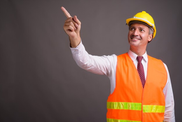 Retrato de hombre trabajador de la construcción contra la pared gris