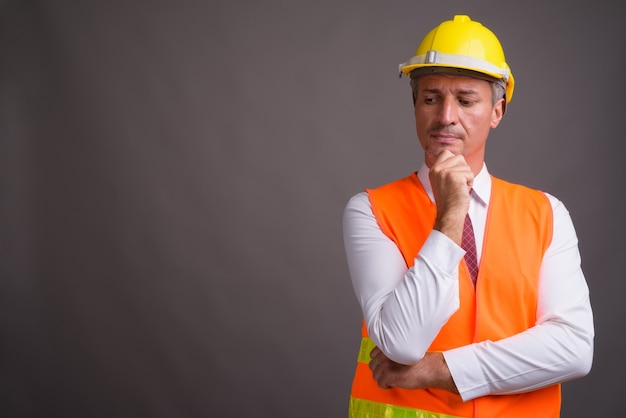 Retrato de hombre trabajador de la construcción contra la pared gris