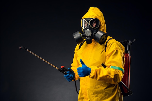 Retrato de un hombre con un traje amarillo de protección química que sostiene un desinfectante rociado.