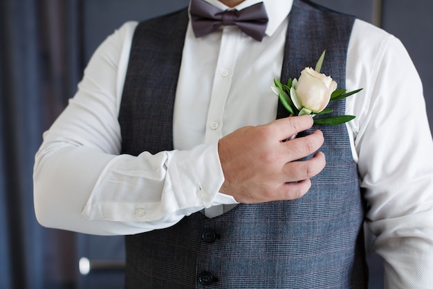 Retrato de hombre en traje oscuro y camisa blanca corrige boutonniere cerrar la mano del novio con ojal