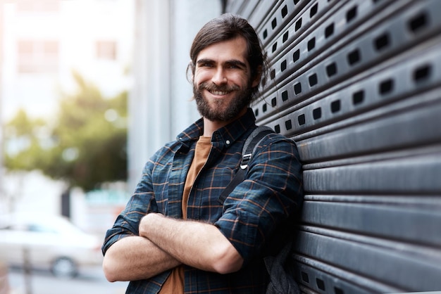 Retrato de hombre y turista con los brazos cruzados en un viaje por la ciudad y un tipo de mochila en Israel Persona masculina viajando y explorando la ciudad urbana para el viaje al aire libre relajarse y destino de vacaciones o vacaciones