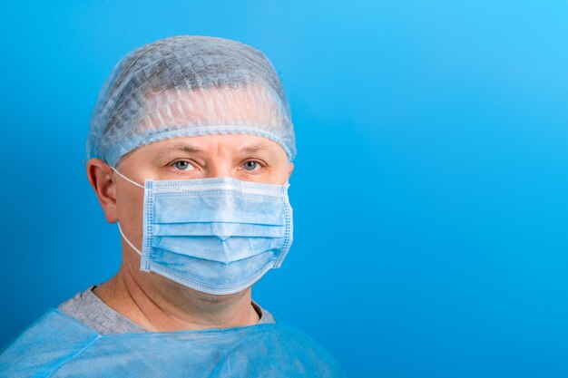 Retrato de hombre con uniforme médico y máscara protectora en azul. Coronavirus y concepto de atención médica con espacio de copia