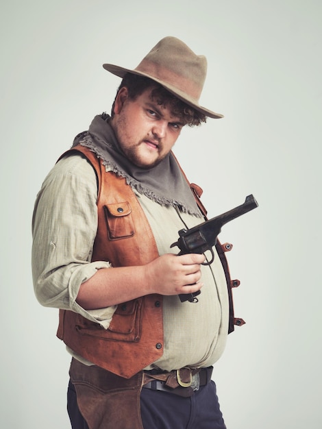 Retrato de hombre y vaquero con un arma confianza y persona en un fondo de estudio blanco modelo de cara y tipo con una pistola y arma de fuego con peligro y advertencia con disfraz de Halloween orgulloso y Texas