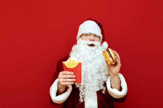 Retrato hombre vestido como Santa Claus con hamburguesa y papas fritas