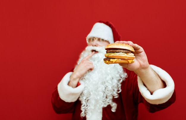 Retrato hombre vestido como Santa Claus sosteniendo burger