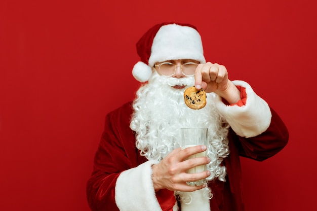 Retrato hombre vestido como Santa Claus sosteniendo un vaso de leche y un plato con galletas de chocolate