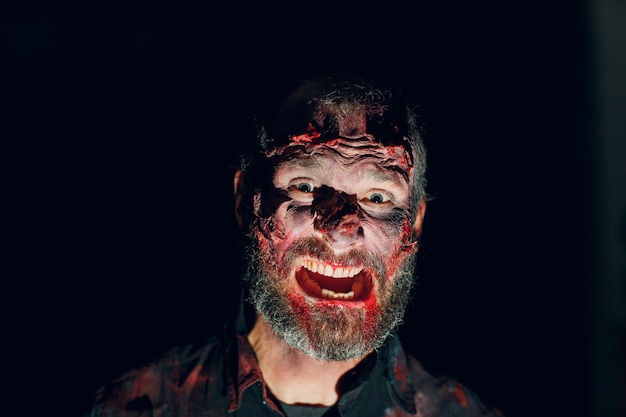 Retrato de hombre zombie en la oscuridad con maquillaje para fiesta de halloween