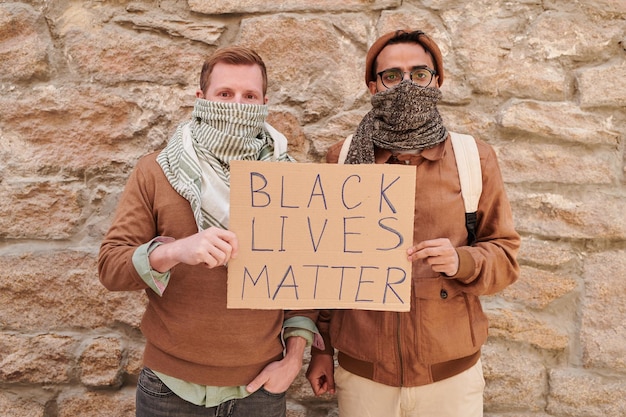 Retrato de hombres negros y blancos con la boca cubierta sosteniendo una pancarta de materia viva negra mientras luchan por los derechos humanos negros en una manifestación