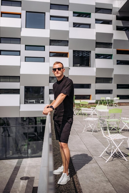 Retrato de hombres en pantalones cortos negros y gafas de sol de camiseta negra en la calle Retrato masculino de verano