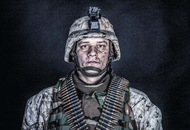 Retrato de hombro de un experimentado soldado del ejército, veterano de conflictos militares, hábil luchador marino con uniforme de camuflaje irregular, casco avanzado y cinturones de munición en el pecho, foto de estudio sobre fondo negro