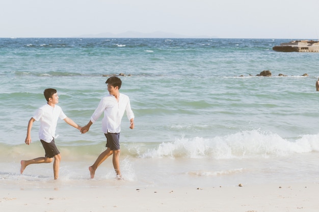 Retrato homossexual jovem casal asiático correndo juntos na praia.