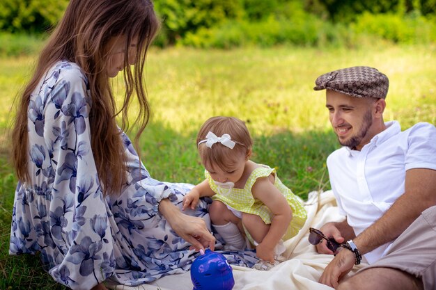 Retrato horizontal de família feliz se divertindo no parque. Pais com filha relaxante ao ar livre.