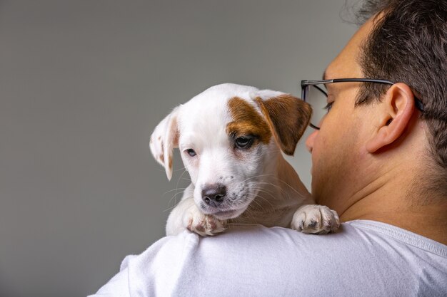 Retrato horizontal de um homem bonito e alegre segurando jack russell terrirer no ombro, com expressão alegre