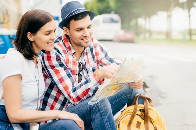 Retrato horizontal do casal feliz, descansando juntos ao ar livre, sentado no banco, olhando no guia da cidade, tendo um sorriso gentil, procurando um lugar para onde ir. Pessoas, férias, conceito de turismo