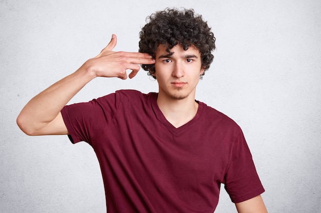 El retrato horizontal de un guapo hombre barbudo con cabello nítido y barba pequeña hace gestos suicidas