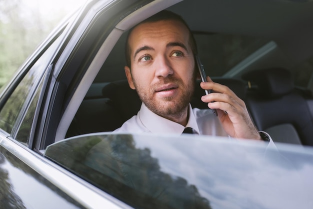 Retrato horizontal de un hombre de negocios hablando por teléfono móvil y mirando por la ventana del auto en un taxi Hombre de negocios de Handosme usando un teléfono inteligente para noticias Concepto de tecnología y negocios