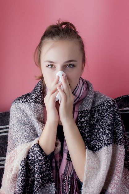 Retrato horizontal joven con un pañuelo y secreción nasal en el perfil, estornudos de gripe, modelo femenino de piel blanca en la pared rosa. Concepto médico y sanitario.