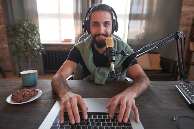 Retrato horizontal de un joven vlogger de Oriente Medio con barba moderna que usa ropa informal sitti