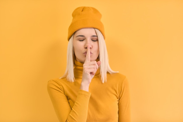 Retrato horizontal de una mujer bonita presionando el dedo contra sus labios diciendo Shh hush pide que se calle con ropa amarilla contra el espacio de copia en blanco de fondo amarillo para su anuncio