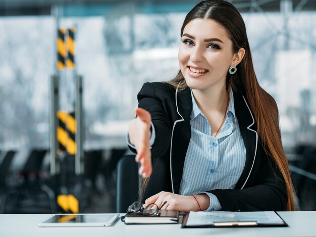 Retrato de HR amigable. Sonriente mujer pasante de pie en el mostrador extender la mano de bienvenida