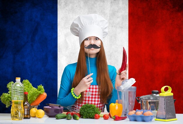 Retrato humorístico de uma mulher com chapéu de chef com bigode de papel segurando a páprica na cozinha
