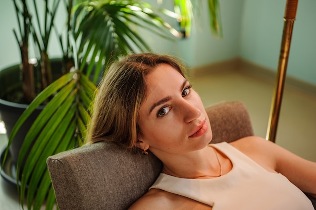 Retrato de una impresionante mujer sentada en una silla cerca de la planta