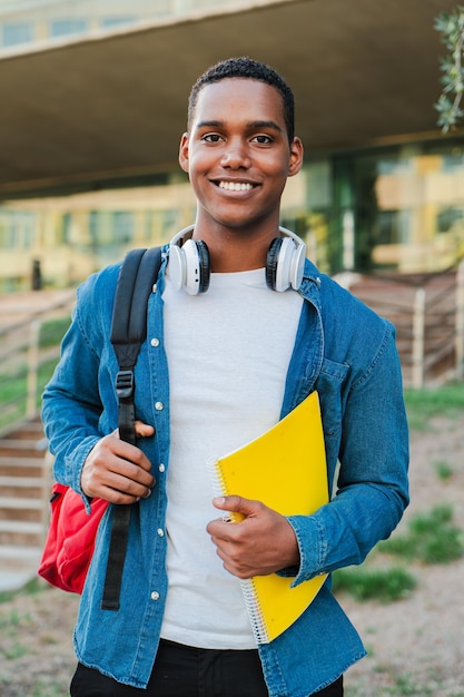 Retrato individual vertical de un joven estudiante afroamericano que lleva una mochila y una nota