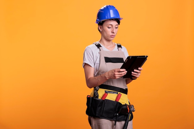 Retrato de una ingeniera de la industria que trabaja con una tableta, buscando inspiración renovadora en línea en un dispositivo inalámbrico. Contratista femenina en overoles usando dispositivo digital electrónico.