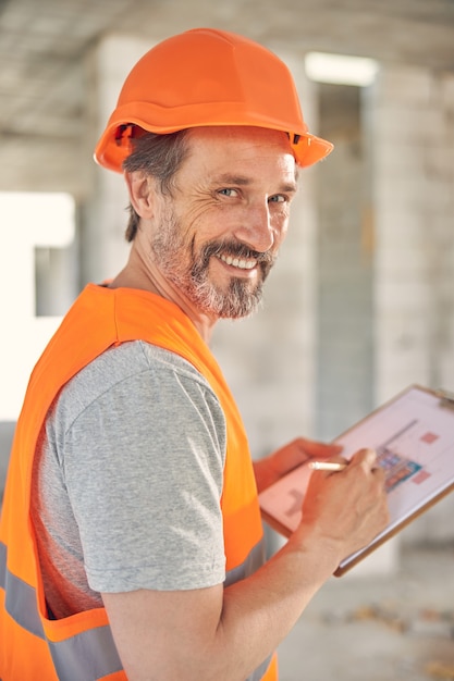 Retrato de un ingeniero alegre con un lápiz y un portapapeles posando para la cámara