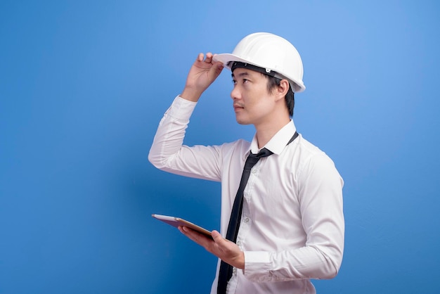 Retrato de un ingeniero confiado que lleva un casco blanco usando una tableta sobre un estudio de fondo azul