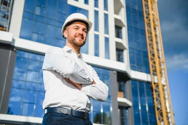 Retrato de un ingeniero contratista masculino sonriente con modelo de lectura de casco en el sitio de construcción.