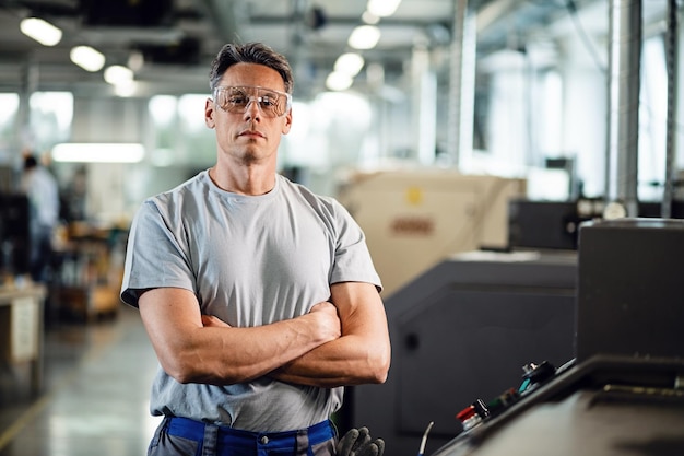 Retrato de ingeniero industrial con los brazos cruzados de pie junto a la máquina CNC y mirando a la cámara