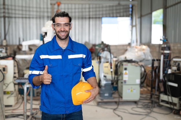 Retrato de ingeniero masculino con casco sonriendo y mostrando los pulgares hacia arriba en la fábrica