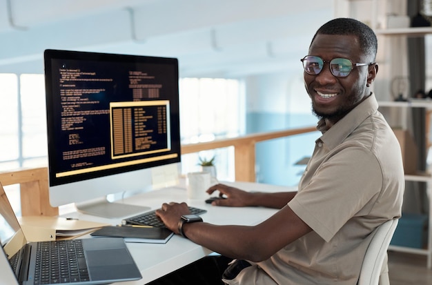 Retrato de un ingeniero de software sonriente que trabaja en una computadora en la oficina de su empresa