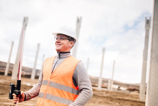 Retrato de ingeniero sonriente en el agrimensor del sitio de construcción usando sistema gps y teodolito en el sitio de construcción de la carretera