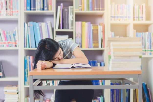 Retrato de inteligente estudiante asiático agotado para leer y hacer investigación en la biblioteca de la universidad