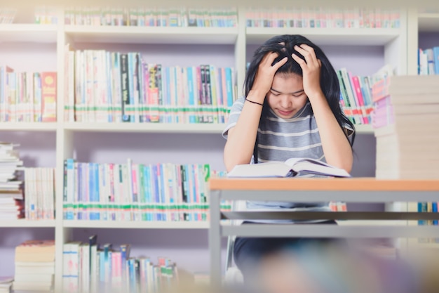 Retrato de inteligente estudiante asiático agotado para leer y hacer investigación en la biblioteca de la universidad