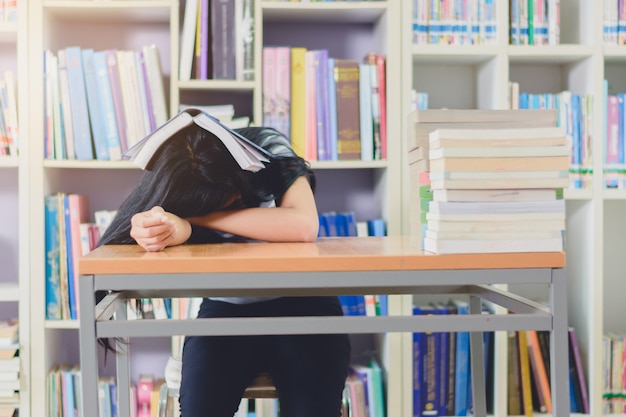 Retrato de inteligente estudiante asiático agotado para leer y hacer investigación en la biblioteca de la universidad